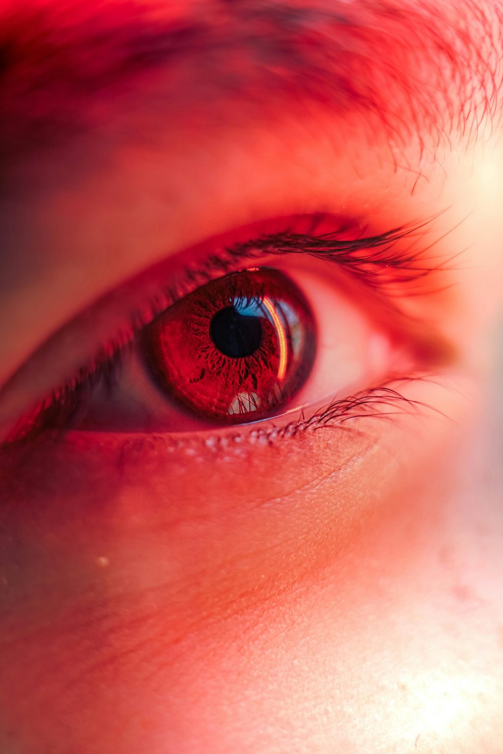 Gros plan de couleur rouge sur un œil humain avec détails de la pupille, de l’iris et des cils environnants.